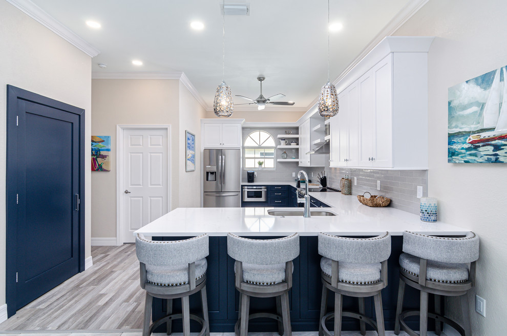 Kitchen - transitional u-shaped medium tone wood floor and brown floor kitchen idea in Miami with an undermount sink, shaker cabinets, white cabinets, gray backsplash, subway tile backsplash, stainless steel appliances, a peninsula and white countertops
