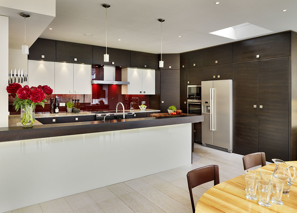 Foto på ett funkis kök och matrum, med släta luckor, vita skåp, rött stänkskydd, glaspanel som stänkskydd, rostfria vitvaror, ljust trägolv och en halv köksö