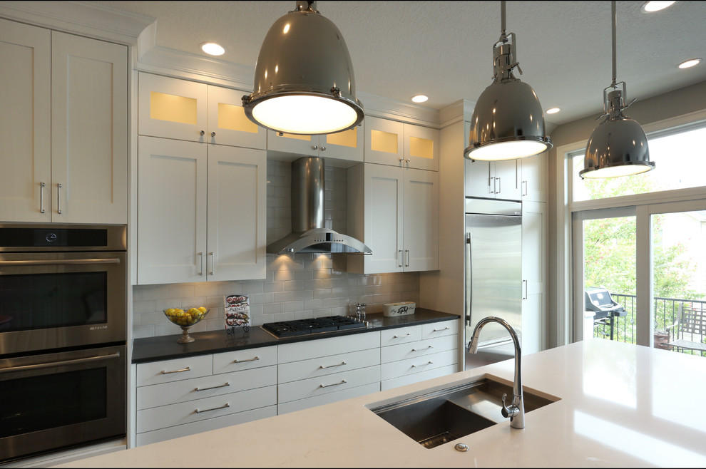 This is an example of a large country single-wall kitchen/diner in Portland with a submerged sink, shaker cabinets, white cabinets, engineered stone countertops, white splashback, metro tiled splashback, stainless steel appliances, dark hardwood flooring and an island.