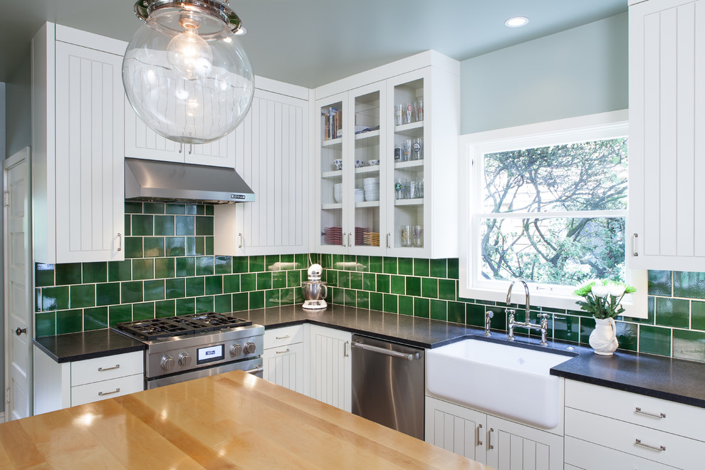 Photo of a medium sized traditional l-shaped enclosed kitchen in Portland with a belfast sink, beaded cabinets, white cabinets, granite worktops, green splashback, ceramic splashback, stainless steel appliances, light hardwood flooring and an island.