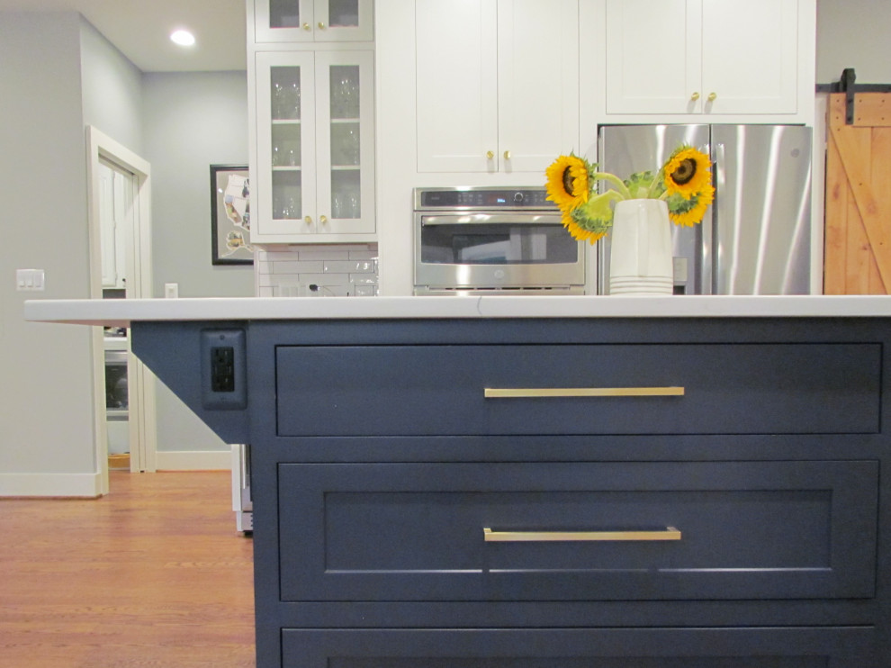 Diseño de cocina comedor campestre grande con fregadero bajoencimera, armarios estilo shaker, puertas de armario azules, encimera de cuarzo compacto, salpicadero blanco, salpicadero de azulejos tipo metro, electrodomésticos de acero inoxidable, suelo de madera en tonos medios, una isla, suelo marrón y encimeras blancas