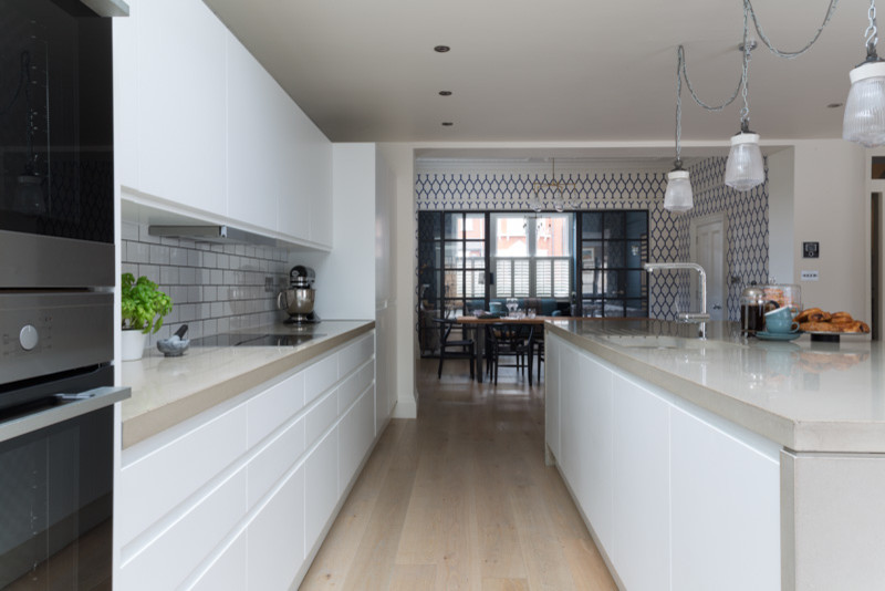 Modern inredning av ett mellanstort linjärt kök med öppen planlösning, med en dubbel diskho, släta luckor, vita skåp, bänkskiva i betong, vitt stänkskydd, stänkskydd i keramik, rostfria vitvaror, ljust trägolv och en köksö