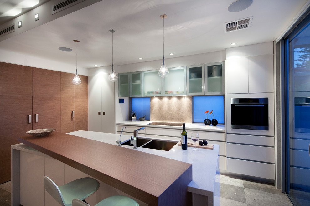 Moderne Küche mit Doppelwaschbecken, flächenbündigen Schrankfronten, weißen Schränken, Küchenrückwand in Beige und Rückwand aus Stein in Sonstige