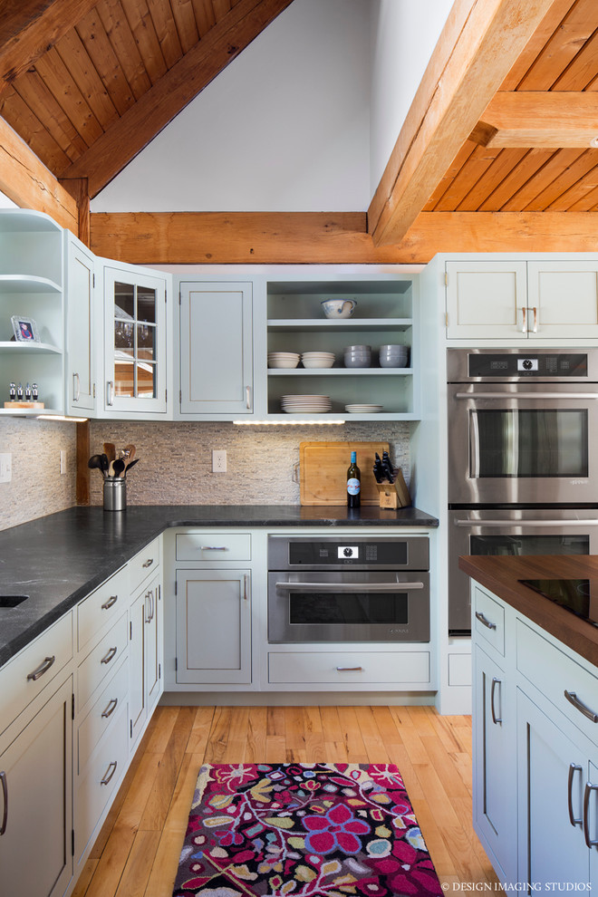 Mid-sized country u-shaped medium tone wood floor kitchen photo in Boston with an undermount sink, shaker cabinets, green cabinets, beige backsplash, stone tile backsplash, stainless steel appliances and an island