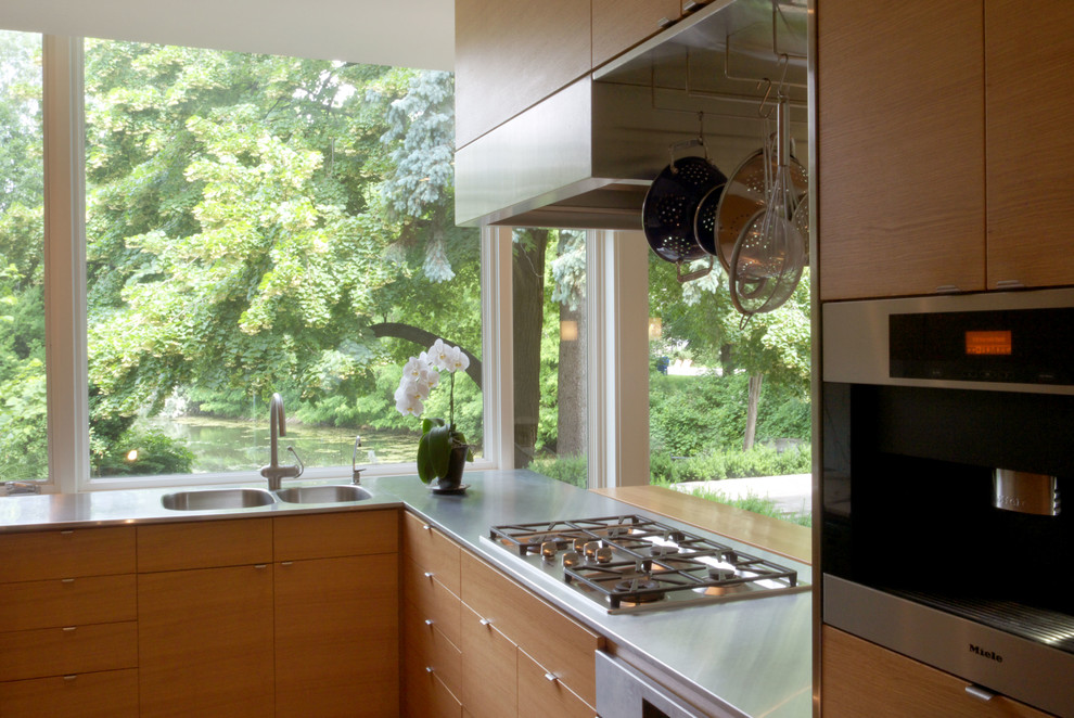 Inredning av ett modernt kök, med en integrerad diskho, släta luckor, skåp i mellenmörkt trä, bänkskiva i rostfritt stål, vitt stänkskydd, stänkskydd i sten och rostfria vitvaror