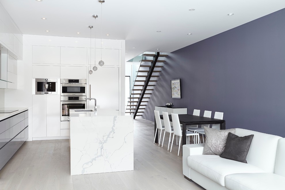 Inspiration for a medium sized contemporary l-shaped open plan kitchen in Toronto with a submerged sink, flat-panel cabinets, white cabinets, engineered stone countertops, white splashback, stone slab splashback, stainless steel appliances, light hardwood flooring, an island and a feature wall.