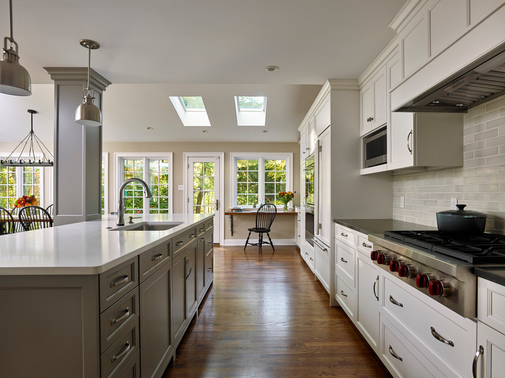 Example of a mid-sized classic galley medium tone wood floor open concept kitchen design in Philadelphia with an undermount sink, recessed-panel cabinets, gray cabinets, quartz countertops, gray backsplash, subway tile backsplash, stainless steel appliances and an island