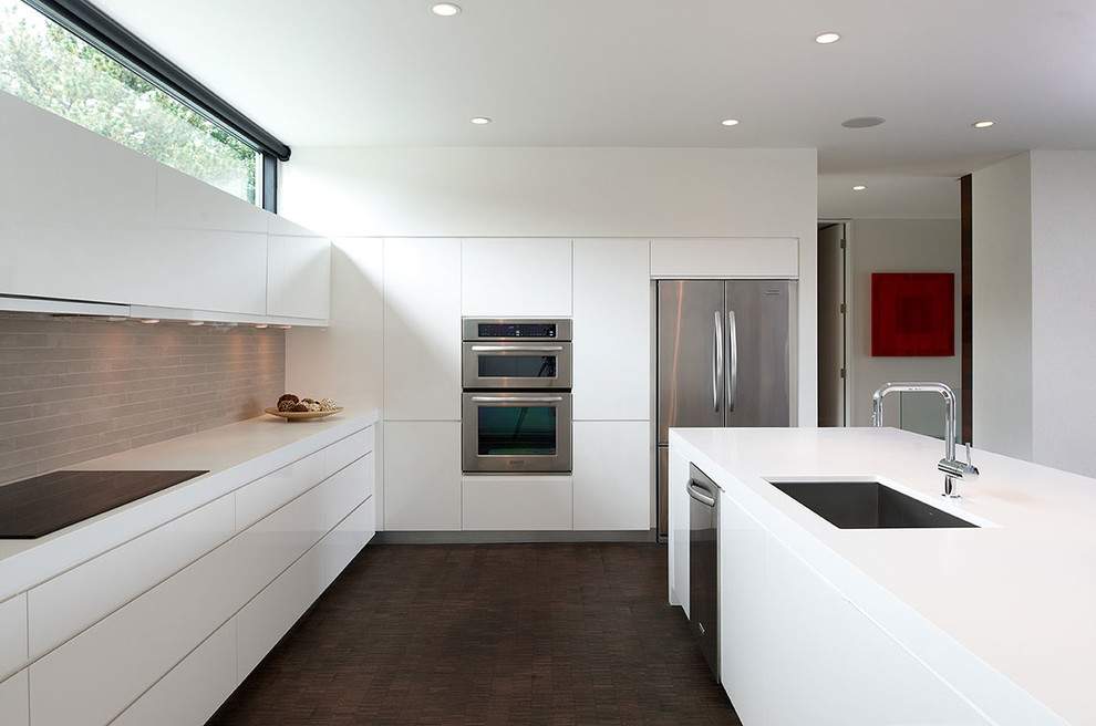 Photo of a medium sized modern l-shaped open plan kitchen in Minneapolis with stainless steel appliances, a submerged sink, flat-panel cabinets, white cabinets, composite countertops, beige splashback, stone tiled splashback, dark hardwood flooring and an island.