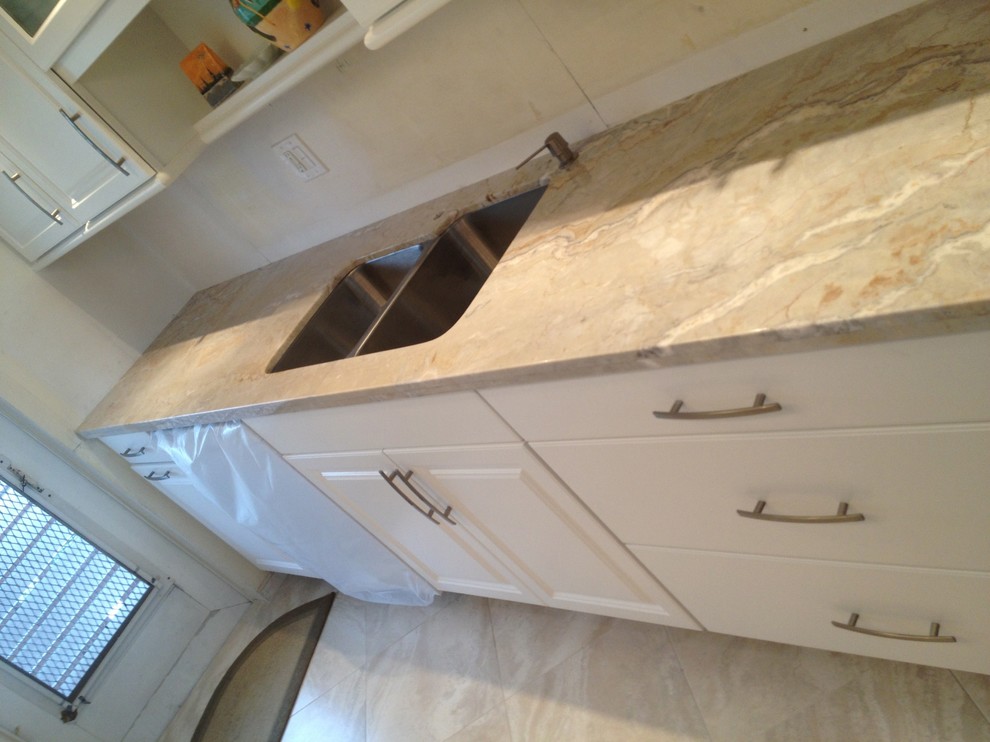 This is an example of a small traditional galley kitchen/diner in Miami with a submerged sink, raised-panel cabinets, white cabinets, quartz worktops, stainless steel appliances, travertine flooring and a breakfast bar.
