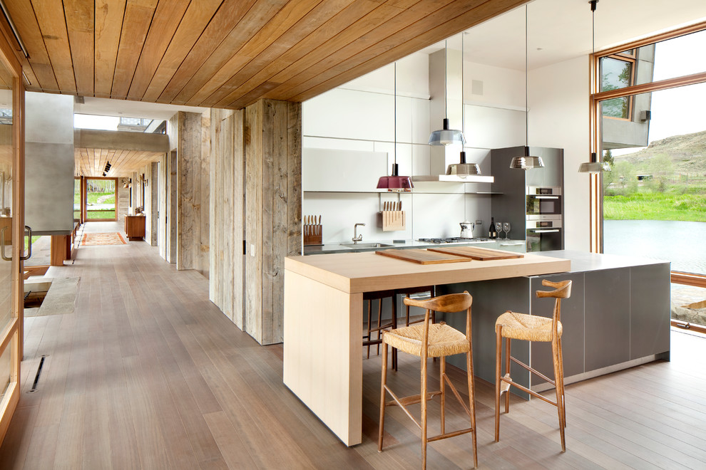 Cette image montre une cuisine design avec un placard à porte plane, des portes de placard grises, un plan de travail en bois et un électroménager en acier inoxydable.