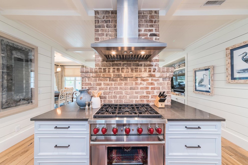 Photo of a large coastal l-shaped kitchen in Atlanta with a belfast sink, recessed-panel cabinets, grey cabinets, composite countertops, stainless steel appliances, light hardwood flooring, an island, brown floors and grey worktops.