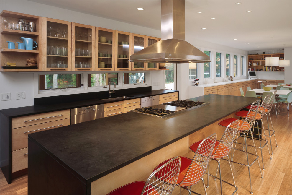 Example of a large trendy light wood floor eat-in kitchen design in New York with an undermount sink, glass-front cabinets, light wood cabinets, solid surface countertops, window backsplash, stainless steel appliances, an island and black countertops