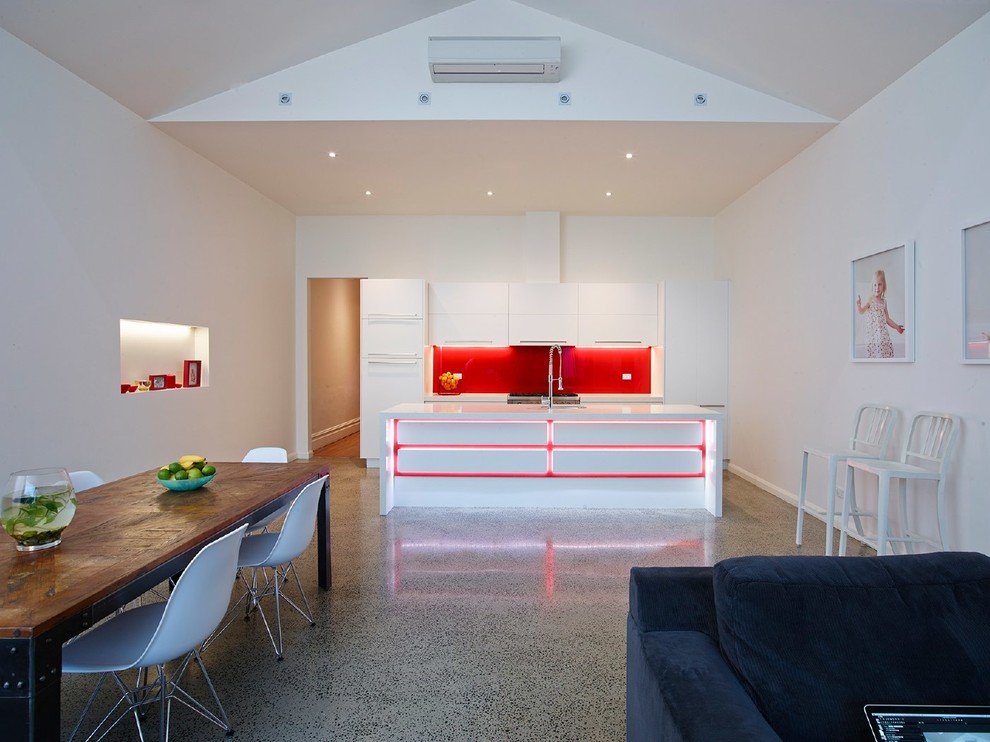Bild på ett funkis kök med öppen planlösning, med vita skåp och rött stänkskydd