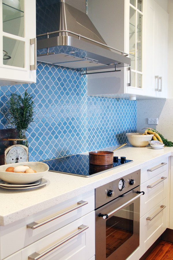 Bild på ett mellanstort funkis kök, med skåp i shakerstil, vita skåp, bänkskiva i kvarts, blått stänkskydd, stänkskydd i keramik, rostfria vitvaror, mellanmörkt trägolv och en halv köksö