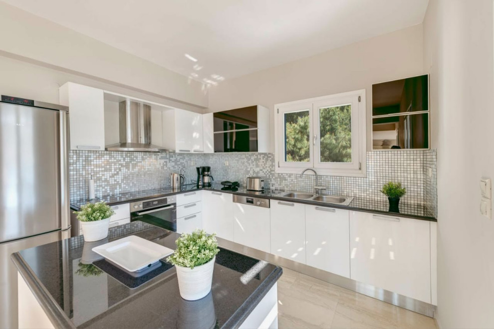 This is an example of a large mediterranean l-shaped open plan kitchen in San Francisco with a built-in sink, flat-panel cabinets, white cabinets, marble worktops, blue splashback, mosaic tiled splashback, stainless steel appliances, marble flooring, an island, beige floors and black worktops.