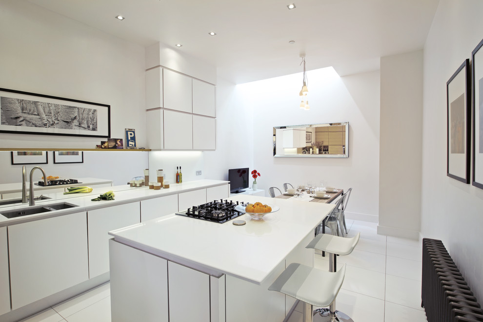 Photo of a medium sized contemporary galley kitchen/diner in London with flat-panel cabinets, white cabinets, ceramic flooring, an island, a double-bowl sink, white splashback and glass sheet splashback.