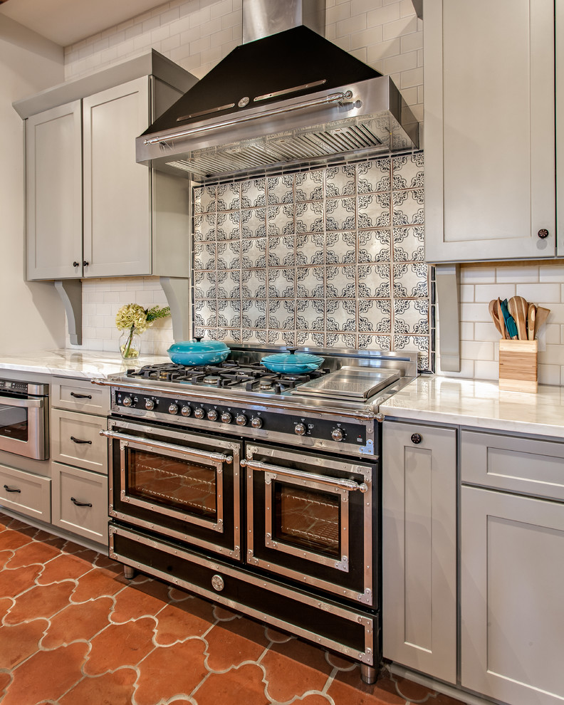 Example of a tuscan terra-cotta tile open concept kitchen design in Nashville with shaker cabinets, gray cabinets, white backsplash, black appliances and an island