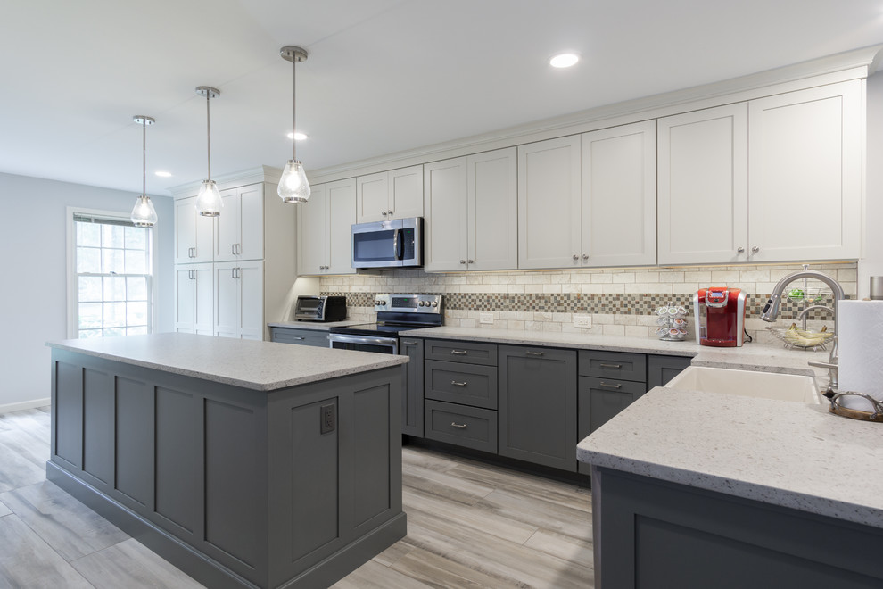 Photo of a large contemporary l-shaped kitchen/diner in Philadelphia with a belfast sink, shaker cabinets, grey cabinets, engineered stone countertops, white splashback, mosaic tiled splashback, stainless steel appliances, porcelain flooring, an island, grey floors and grey worktops.