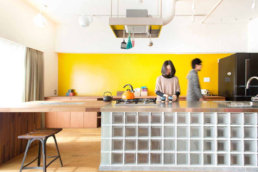 東京23区にあるインダストリアルスタイルのおしゃれなアイランドキッチン (フラットパネル扉のキャビネット、中間色木目調キャビネット、黄色いキッチンパネル、黒い調理設備、無垢フローリング) の写真