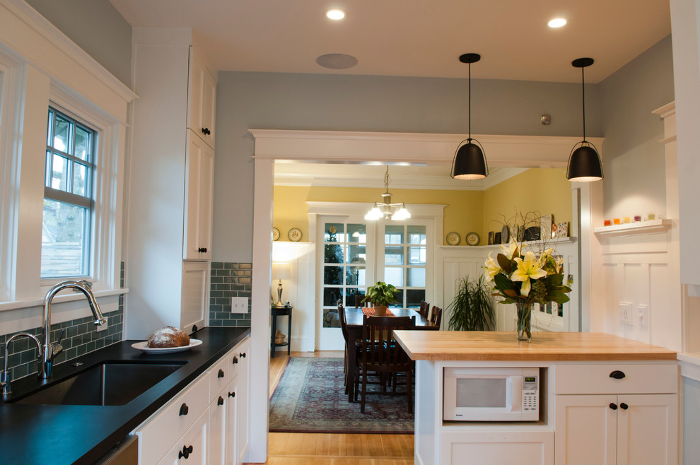 Mid-sized arts and crafts u-shaped light wood floor eat-in kitchen photo in Portland with an undermount sink, shaker cabinets, white cabinets, wood countertops, glass tile backsplash, stainless steel appliances and a peninsula