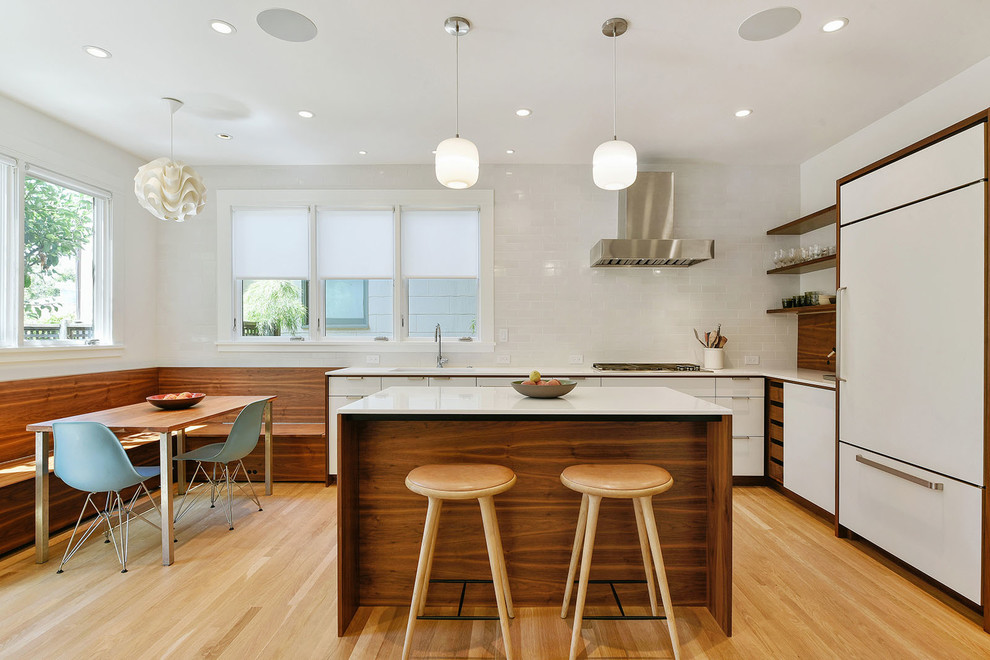 Offene Moderne Küche in L-Form mit flächenbündigen Schrankfronten, dunklen Holzschränken, Rückwand aus Keramikfliesen, Elektrogeräten mit Frontblende, hellem Holzboden, orangem Boden, Küchenrückwand in Weiß und Kücheninsel in San Francisco