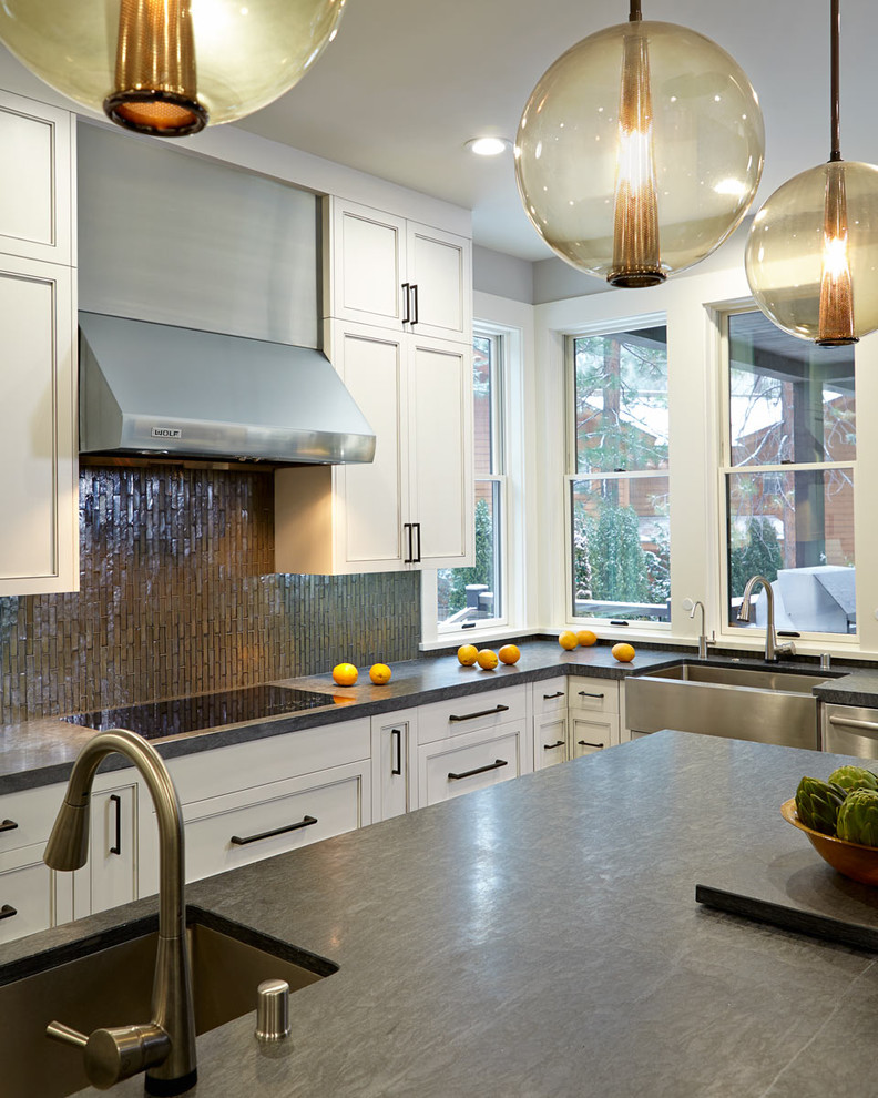 Example of a large trendy l-shaped dark wood floor eat-in kitchen design in San Francisco with a farmhouse sink, recessed-panel cabinets, white cabinets, soapstone countertops, gray backsplash, glass tile backsplash, stainless steel appliances and an island