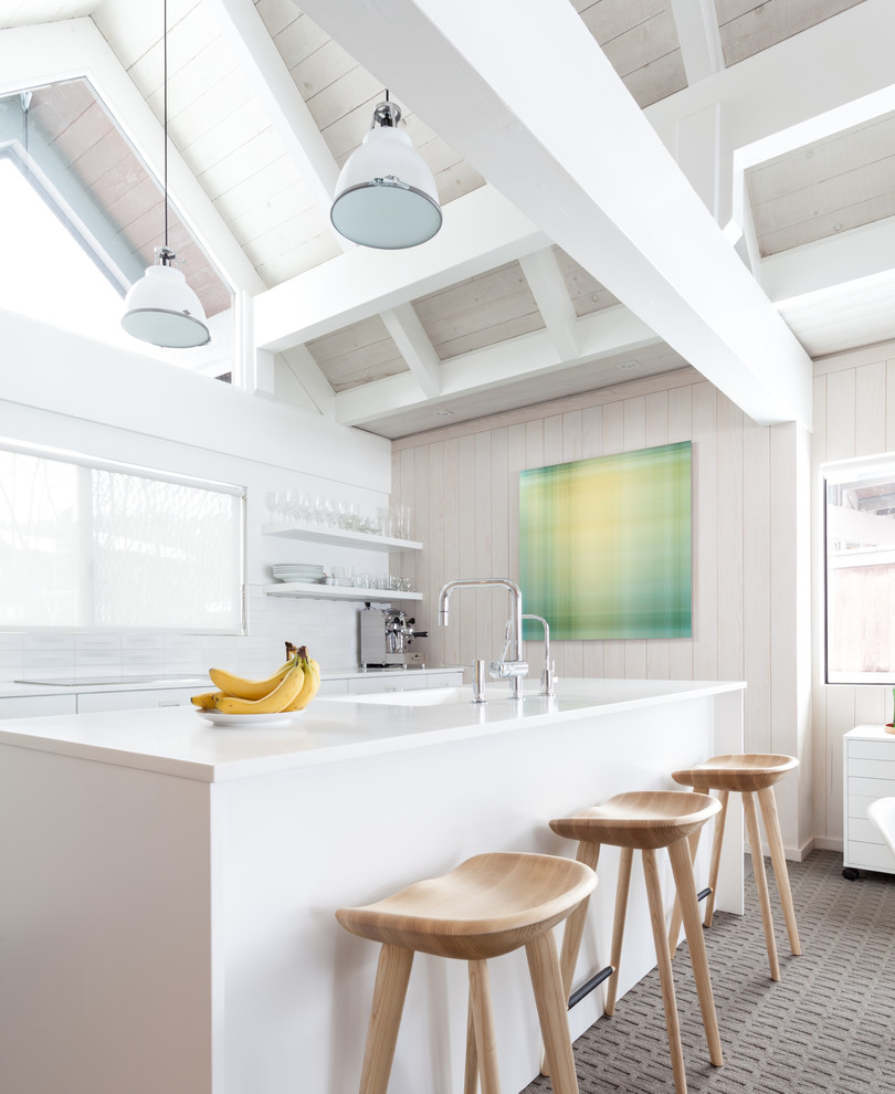 На фото: прямая кухня в белых тонах с отделкой деревом в скандинавском стиле с монолитной мойкой, плоскими фасадами, белыми фасадами, белым фартуком, ковровым покрытием, островом, серым полом и белой столешницей