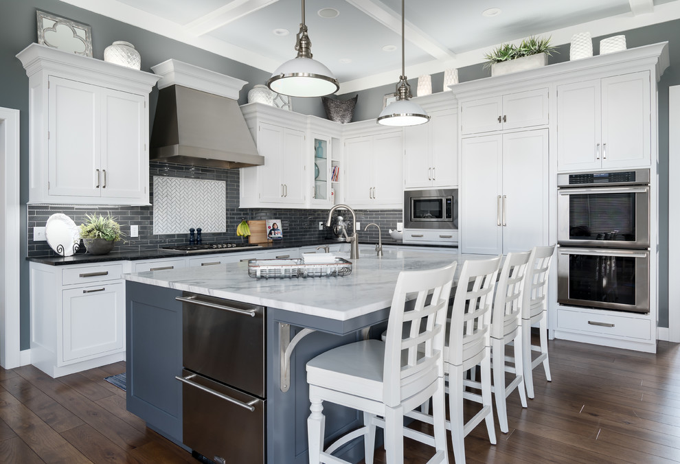 Idées déco pour une cuisine classique en L avec un placard à porte shaker, des portes de placard blanches, une crédence multicolore, un électroménager en acier inoxydable, parquet foncé, îlot, un sol marron et plan de travail noir.