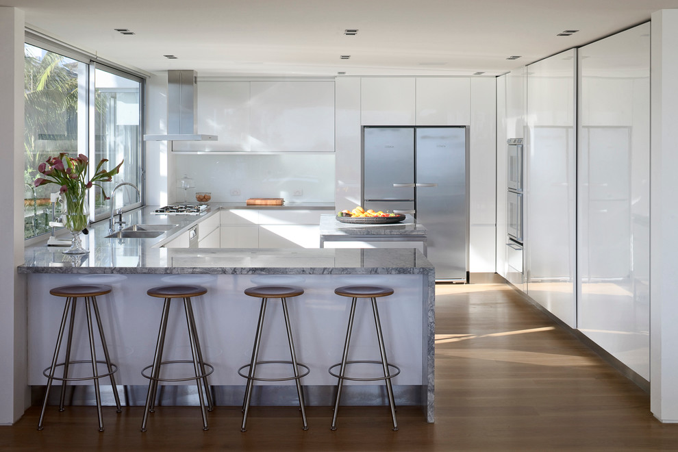Inspiration for a contemporary u-shaped medium tone wood floor kitchen remodel in Auckland with a double-bowl sink, flat-panel cabinets, white cabinets, white backsplash, stainless steel appliances and a peninsula