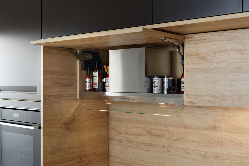 Foto på ett litet funkis brun linjärt kök och matrum, med en enkel diskho, luckor med infälld panel, bruna skåp, laminatbänkskiva, brunt stänkskydd, stänkskydd i trä, svarta vitvaror och en köksö