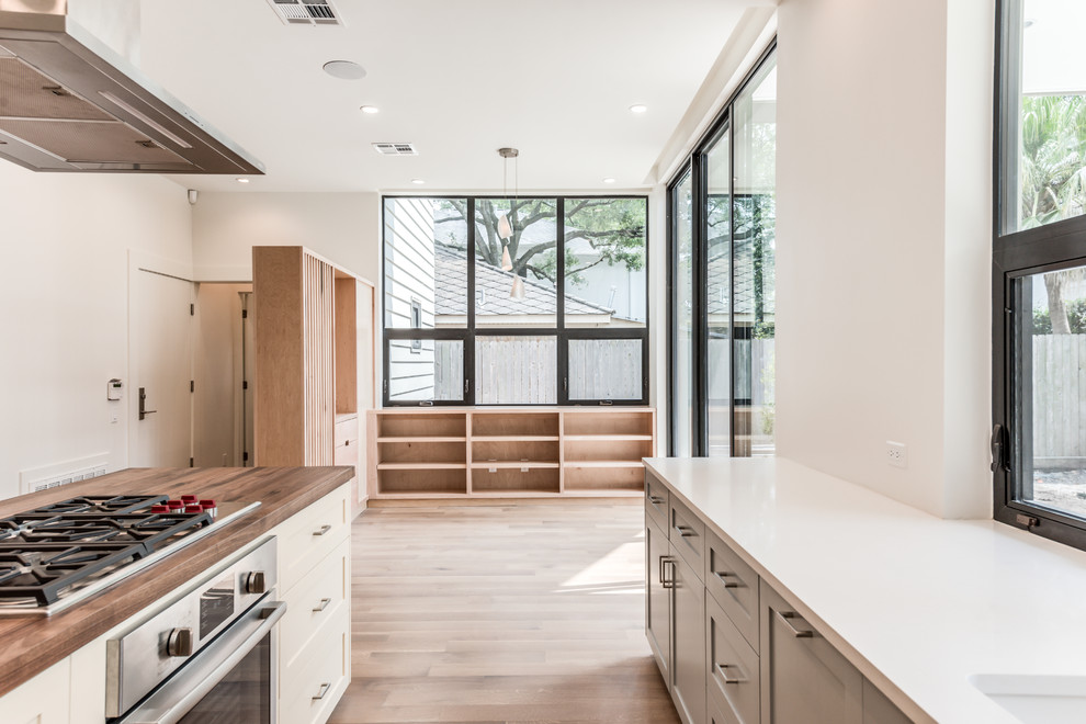Mid-sized trendy u-shaped light wood floor and brown floor enclosed kitchen photo in Houston with an undermount sink, shaker cabinets, white cabinets, solid surface countertops, blue backsplash, terra-cotta backsplash, stainless steel appliances, an island and white countertops