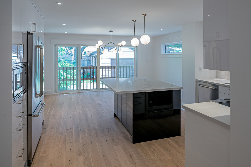 Small traditional l-shaped kitchen/diner in Toronto with a submerged sink, flat-panel cabinets, white cabinets, engineered stone countertops, beige splashback, ceramic splashback, stainless steel appliances, light hardwood flooring, an island, brown floors and white worktops.