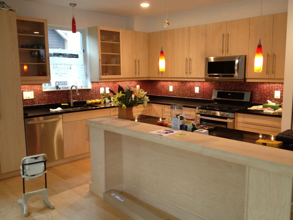 Cette image montre une cuisine minimaliste en bois clair de taille moyenne avec un évier 1 bac, un placard à porte plane, un plan de travail en surface solide, une crédence rouge, une crédence en mosaïque, parquet clair et un sol marron.