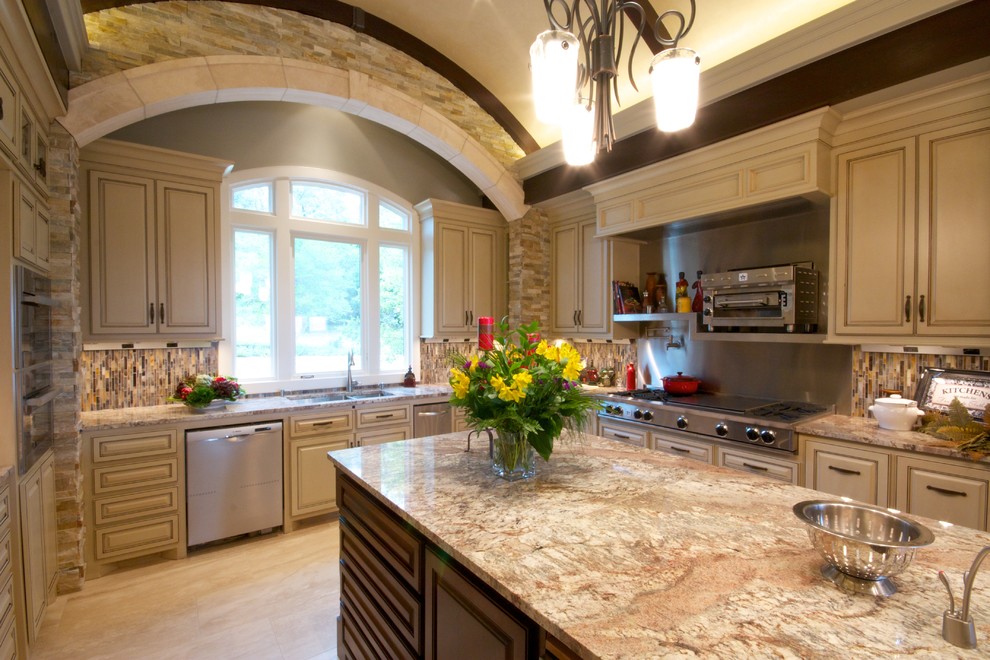 Klassisk inredning av ett mycket stort kök, med en undermonterad diskho, luckor med upphöjd panel, skåp i slitet trä, granitbänkskiva, flerfärgad stänkskydd, rostfria vitvaror och travertin golv