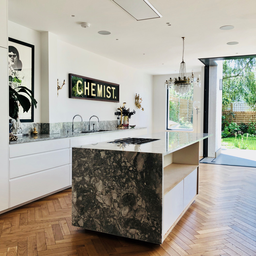 Moderne Küche mit flächenbündigen Schrankfronten, weißen Schränken, Marmor-Arbeitsplatte, hellem Holzboden, Kücheninsel, beigem Boden, Küchenrückwand in Grau und grauer Arbeitsplatte in London
