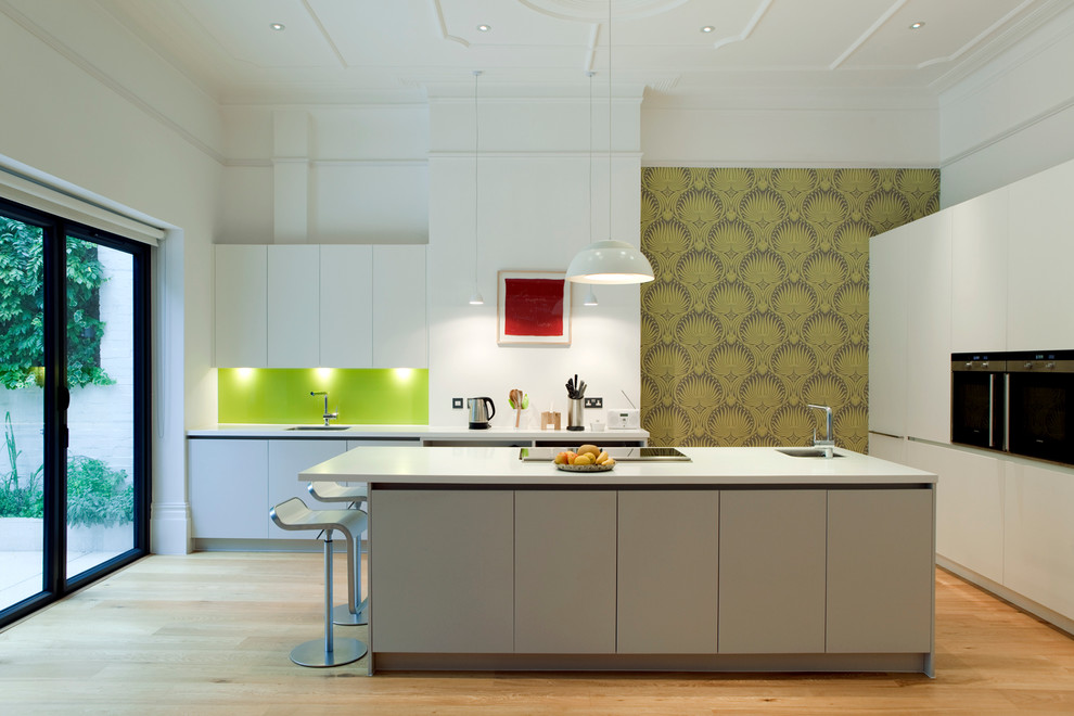 Cette image montre une cuisine design avec un placard à porte plane, des portes de placard blanches, îlot et papier peint.
