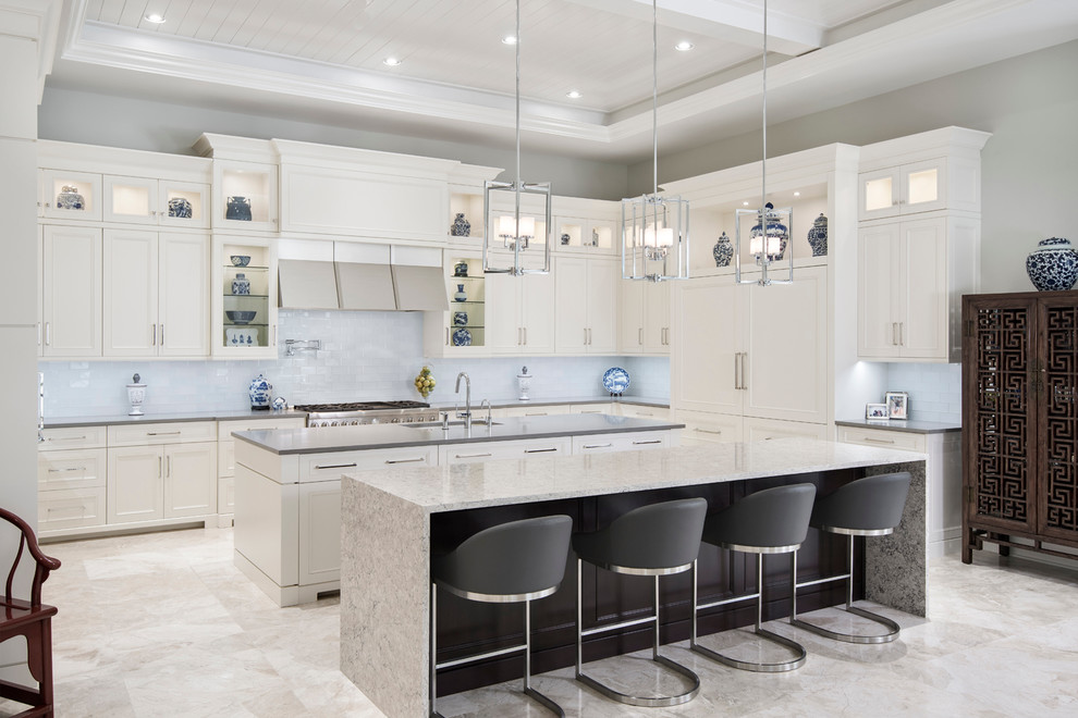 Example of a mid-sized transitional l-shaped travertine floor open concept kitchen design in Miami with a single-bowl sink, recessed-panel cabinets, white cabinets, granite countertops, white backsplash, glass tile backsplash, paneled appliances and two islands