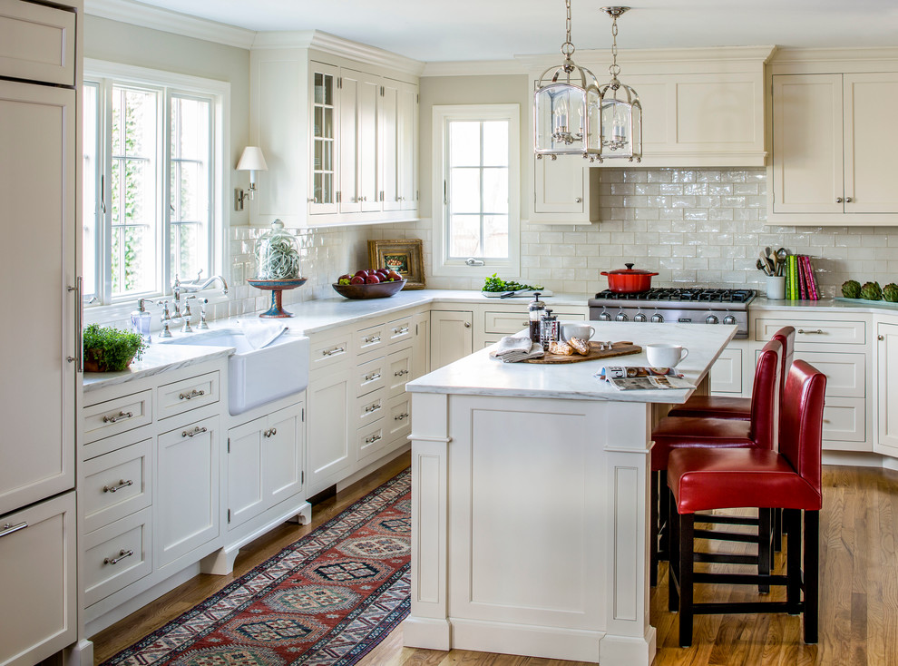 Design ideas for a traditional l-shaped kitchen in New York with a belfast sink, shaker cabinets, white cabinets, marble worktops, white splashback, metro tiled splashback, integrated appliances, medium hardwood flooring and an island.