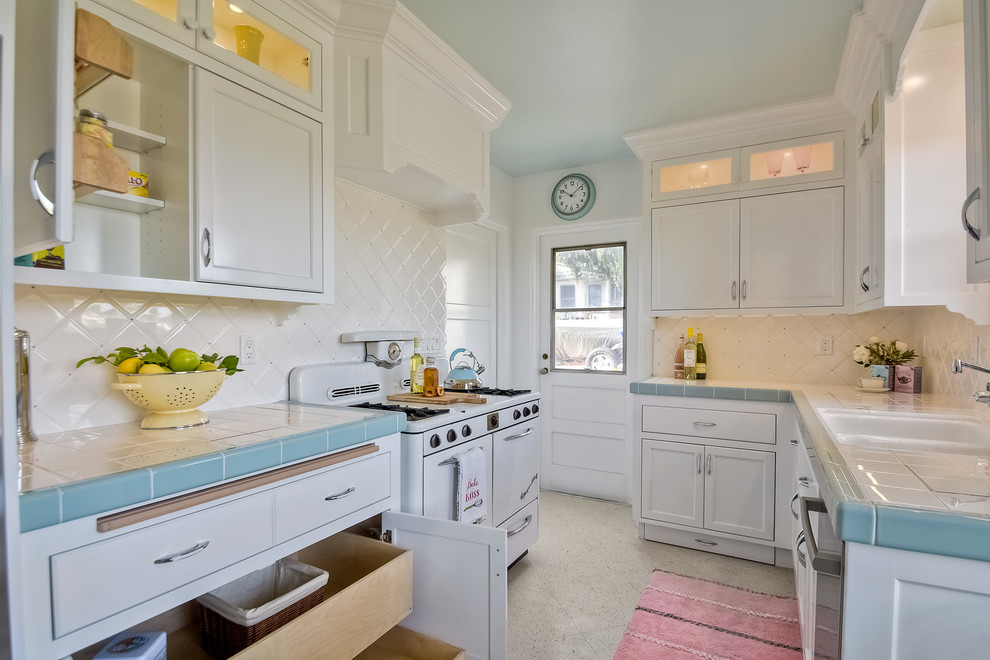 Inspiration for a medium sized traditional galley enclosed kitchen in San Diego with a double-bowl sink, recessed-panel cabinets, white cabinets, tile countertops, white splashback, ceramic splashback, white appliances, terrazzo flooring and no island.