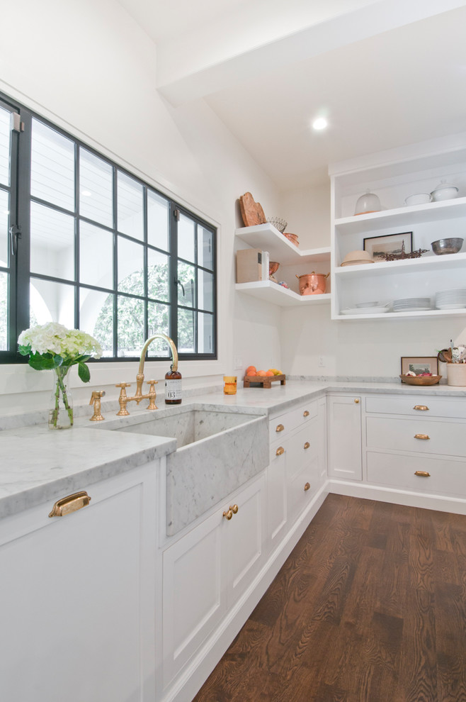 Large classic u-shaped kitchen/diner in Los Angeles with a belfast sink, recessed-panel cabinets, white cabinets, marble worktops, white splashback, marble splashback, black appliances, dark hardwood flooring, an island, brown floors and white worktops.