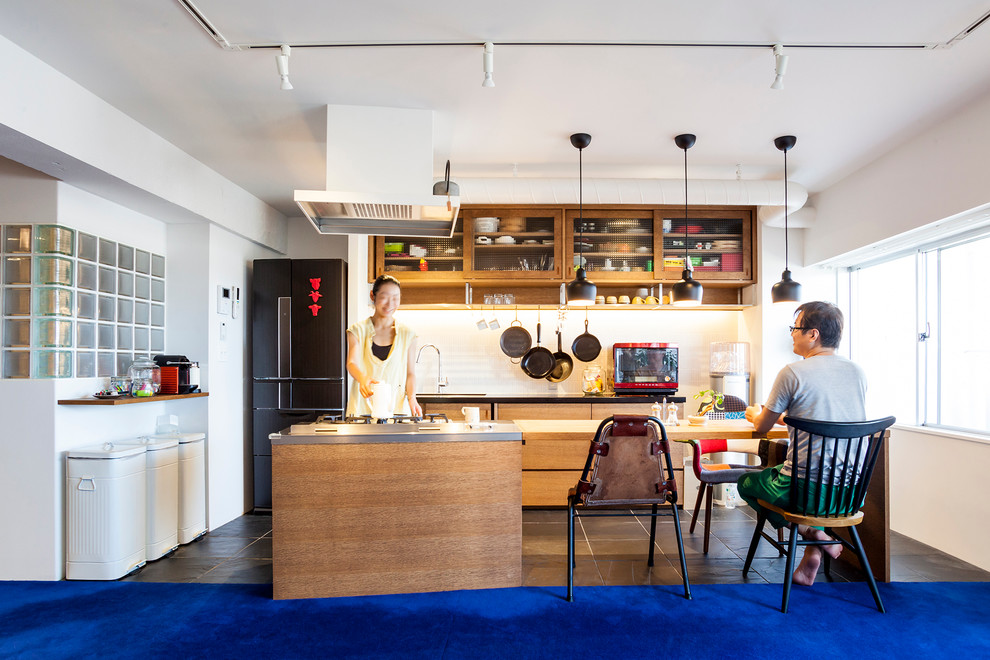 東京23区にある中くらいなおしゃれなキッチン (アンダーカウンターシンク、フラットパネル扉のキャビネット、中間色木目調キャビネット、ステンレスカウンター、白いキッチンパネル、黒い調理設備、スレートの床) の写真