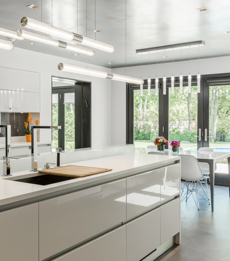 Example of a large minimalist u-shaped concrete floor enclosed kitchen design in New York with an undermount sink, flat-panel cabinets, white cabinets, quartz countertops, gray backsplash, glass sheet backsplash, stainless steel appliances and an island