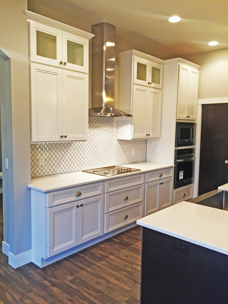 Modern inredning av ett mellanstort kök, med en rustik diskho, luckor med infälld panel, vita skåp, granitbänkskiva, vitt stänkskydd, stänkskydd i keramik, rostfria vitvaror, mörkt trägolv och en köksö