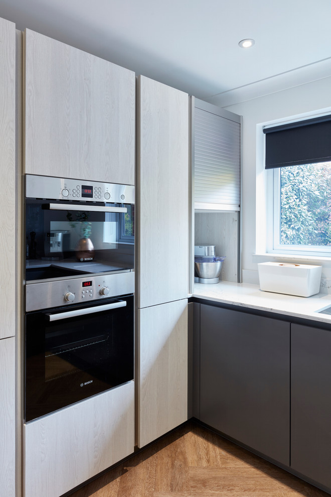 Bild på ett mellanstort funkis kök, med en nedsänkt diskho, släta luckor, grå skåp, bänkskiva i kvartsit, grått stänkskydd, glaspanel som stänkskydd, integrerade vitvaror, linoleumgolv och en halv köksö