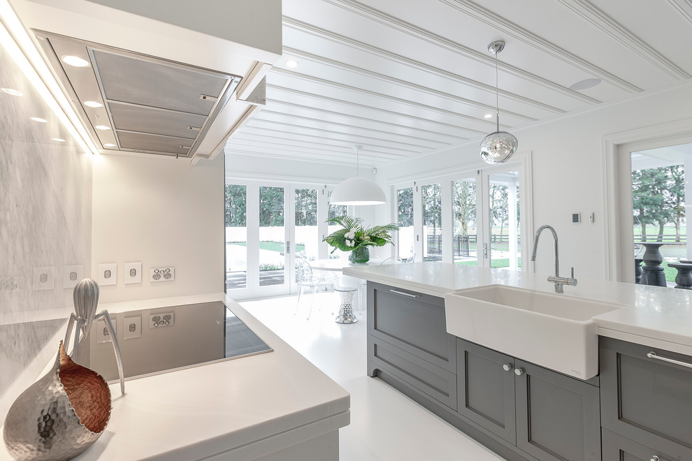 This is an example of an expansive traditional galley kitchen/diner in Auckland with a belfast sink, recessed-panel cabinets, white cabinets, composite countertops, multi-coloured splashback, stone slab splashback, black appliances, painted wood flooring and an island.