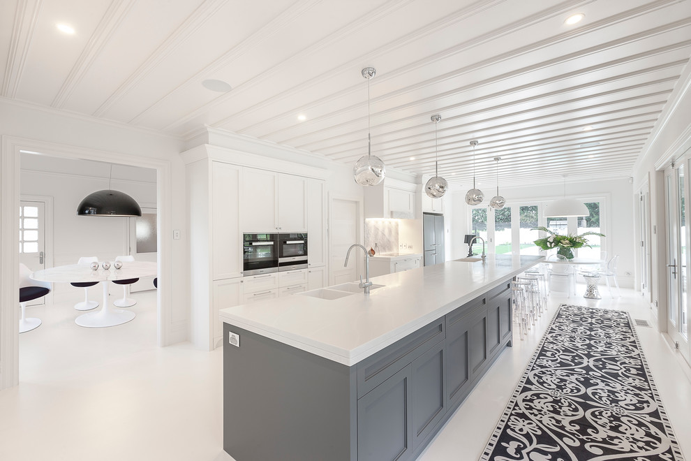 Expansive classic galley kitchen/diner in Hamilton with a belfast sink, recessed-panel cabinets, white cabinets, composite countertops, multi-coloured splashback, stone slab splashback, black appliances and an island.