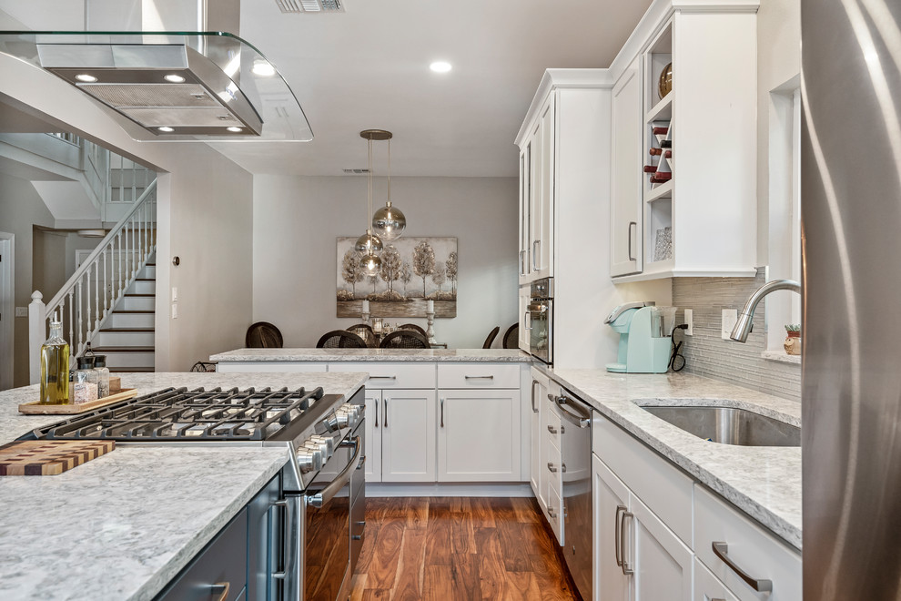 Example of a large beach style l-shaped medium tone wood floor and brown floor open concept kitchen design in Tampa with an undermount sink, shaker cabinets, white cabinets, quartz countertops, gray backsplash, glass tile backsplash, stainless steel appliances, an island and gray countertops