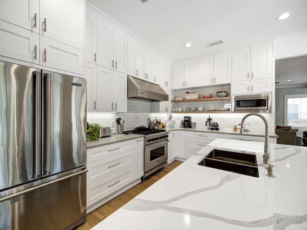 Inspiration for a large transitional l-shaped medium tone wood floor and brown floor kitchen remodel in Tampa with an undermount sink, white cabinets, quartz countertops, white backsplash, subway tile backsplash, stainless steel appliances, an island, gray countertops and shaker cabinets