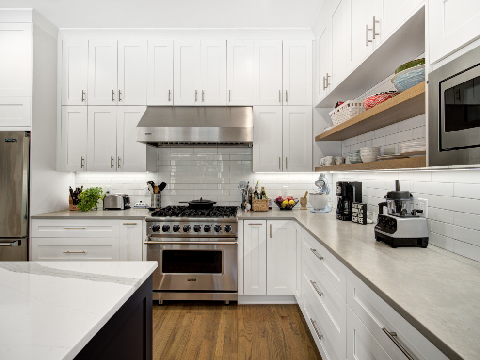 Foto på ett stort funkis grå kök, med en undermonterad diskho, luckor med infälld panel, vita skåp, bänkskiva i kvarts, vitt stänkskydd, stänkskydd i tunnelbanekakel, rostfria vitvaror, mellanmörkt trägolv, en köksö och brunt golv