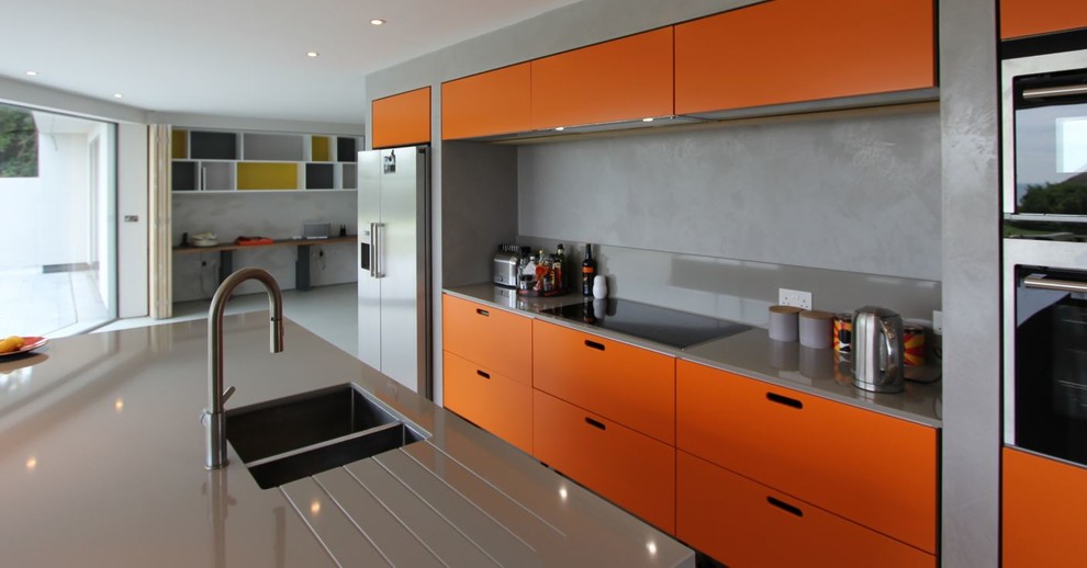 Geräumige Moderne Wohnküche in L-Form mit Unterbauwaschbecken, flächenbündigen Schrankfronten, orangefarbenen Schränken, Küchenrückwand in Grau, Küchengeräten aus Edelstahl, Porzellan-Bodenfliesen und Kücheninsel in Sussex